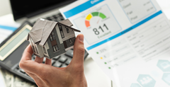 Model house held by a hand and a credit score. Person thinking about how to improve their credit score.